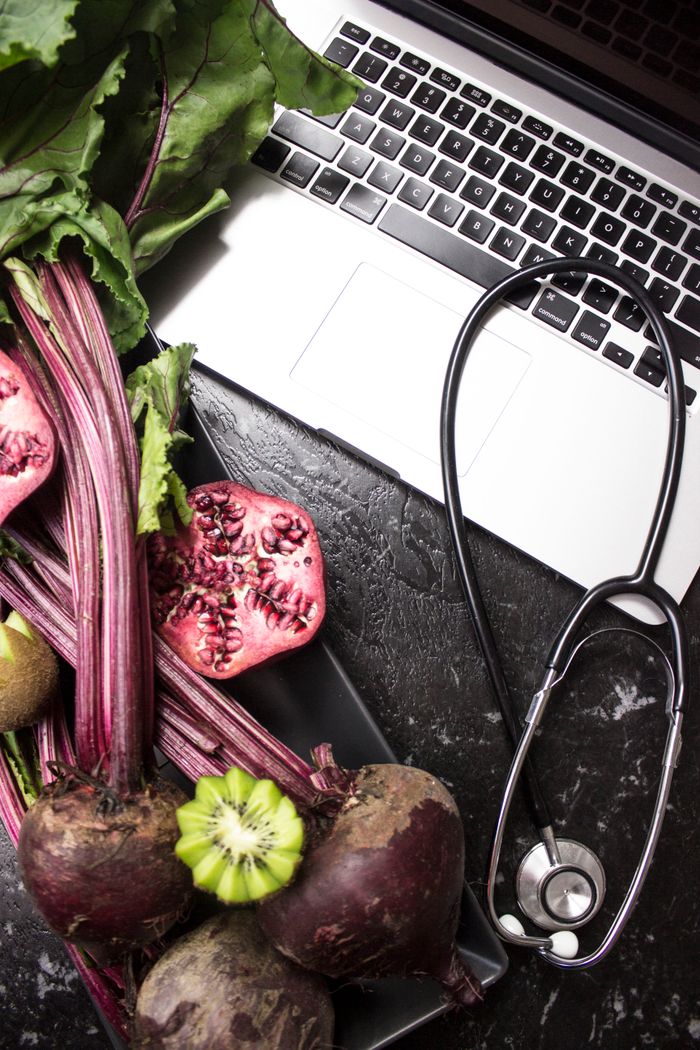Flat lay of fresh vegetables, fruits, stethoscope, and a laptop promoting healthy lifestyle